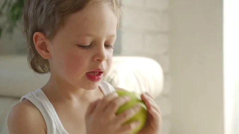 6 year old boy eating green apple and try pull out baby teeth Видео 107933813