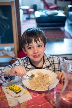 6 year old boy eats rice at the kitchen table in the morning still in his paj Foto stock