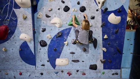 6-year-old boy engaged in bouldering on a vibrant indoor climbing wall. Focused Stock Footage 291978216