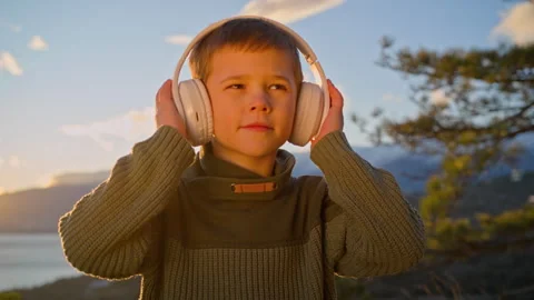 A 6-year-old boy enjoys listening to music while wearing headphones at sunset. Stock Footage 276964881