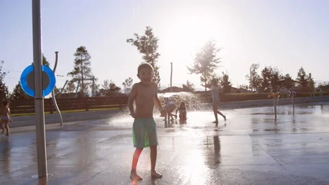 6 year old boy gets covered with huge deluge of water at splash pad slow motion Stock Footage 233944191