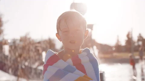 6 year old boy looks to camera at splash pad, overtaken by powerful sun flare Stock Footage 233944859