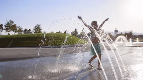 6 year old boy playfully splashes through water arches at splash pad Stock Footage 233939284