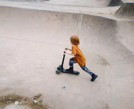 A 6-year-old boy with red hair rides a scooter in the skate park Stock Photos