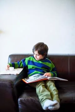 6 year old boy sitting on the sofa reads a book Stock Photos