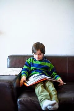 6 year old boy sitting on the sofa reads a book Foto stock