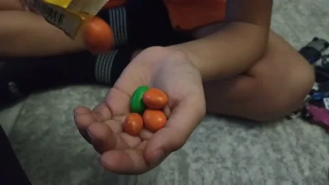 A 6 years old boy pours colored candies out of a bag onto his palm Stock Footage 221084329