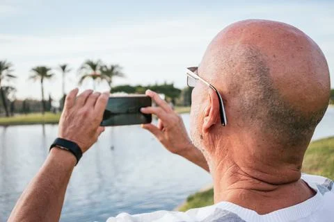65-year-old man taking a photo with a smartphone in a park Stock Photos