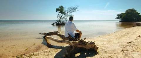 6K - Man Sitting on a Log by the Ocean Stock Footage 125967821