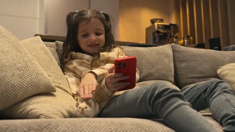 A 7-8 year old cute girl in casual outfit is sitting on a couch with pet. Stock Footage 299708890