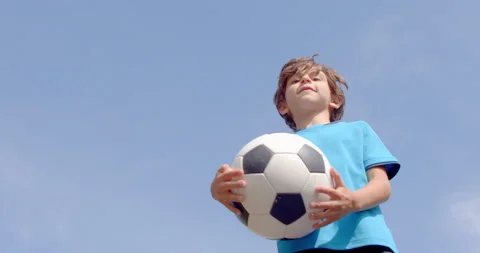 A 7-8 years old boy in football equipment and a ball in hand having fun jumping Stock Footage 161952481