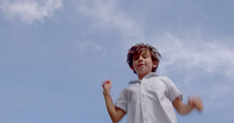 A 7-8 years old boy having fun jumping at trampoline on the blue sky background Stock Footage 161957399