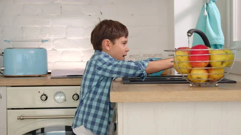 7-8 years old boy washes an apple in the sink of a modern light kitchen Stock Footage 171094357