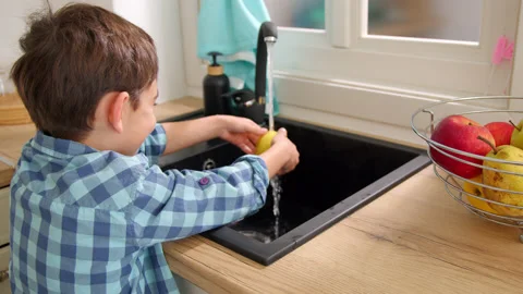 7-8 years old boy washes an apple in the sink of a modern light kitchen Stock Footage 171094411