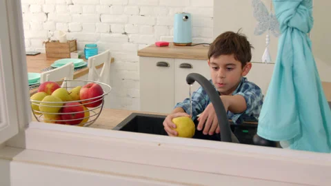 7-8 years old boy washes an apple in the sink of a modern light kitchen Stock Footage 171094723