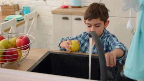 7-8 years old boy washes an apple in the sink of a modern light kitchen Stock Footage 171094945