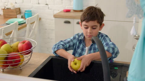 7-8 years old boy washes an apple in the sink of a modern light kitchen Stock Footage 171095221