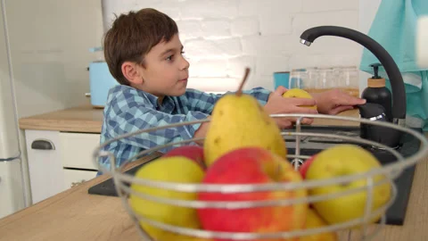 7-8 years old boy washes an apple in the sink of a modern light kitchen Stock Footage 171095394