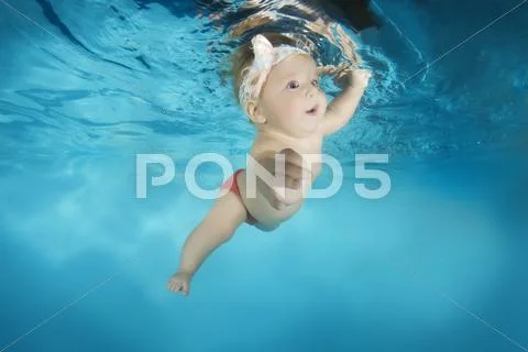 7 months infant girl learning to swim underwater in waterbaby class in the pool Stock Photos