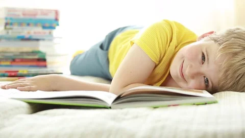 7 year old boy with a book on the bed. Portrait of a cheerful schoolboy with a b Stock Footage 78071187