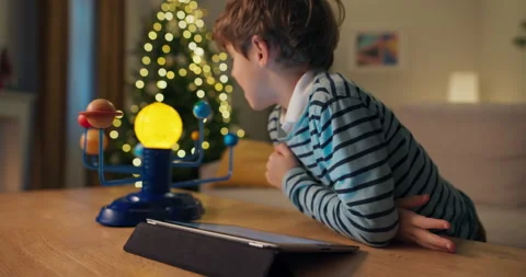 A 7-year-old boy with brown hair looks at pictures of planets on tablet and Stock Footage 210482559