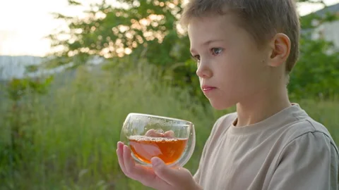 A 7-year-old boy is enjoying a cup of hot tea outdoors. Stock Footage 277103795