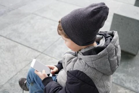 7 year old boy looking at smartphone outdoors in winter Stock Photos