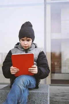7 year old boy reading on tablet pc computer outdoors in winter Stock Photos