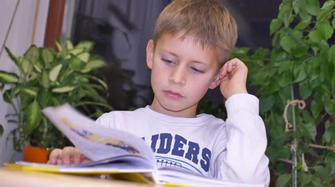 7-year-old cute boy reading a book while sitting at table Stock Footage 43119989