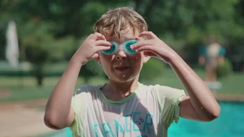 7 yeard old boy puts on goggles in front of swimming pool on hot summer day 스톡 동영상 248078602