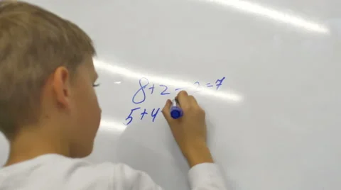7-years old boy writes on a blackboard mathematical examples and solve them Stock Footage 43120540