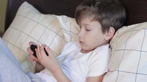 7 years old kid using gadget while laying in bed Stock Footage 161840852