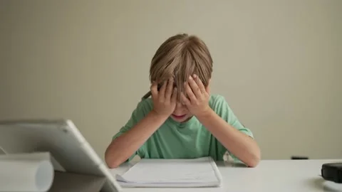7 yeas old boy sitting at table in room and crying while working on hard Stock Footage 195785711