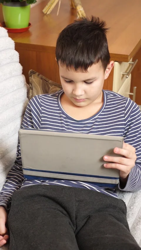 72A boy plays games on a tablet while sitting on the couch. Video stock 313598513