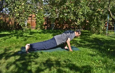 A 76-year-old man is doing push-ups in the garden. Stock Photos