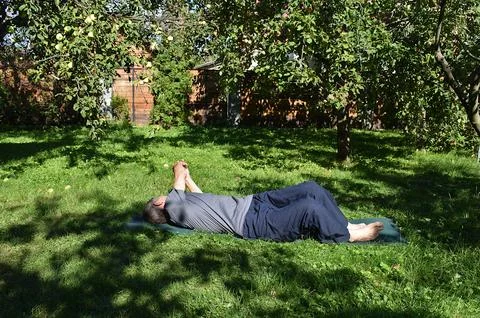 A 76-year-old man performs a twisting exercise on a garden lawn. 스톡 사진