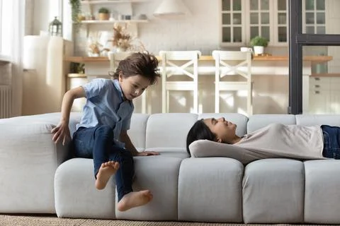 7s boy having fun while Asian mother relaxing on couch Stock Photos