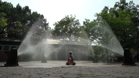 8-11-26, Brooklyn, NY, USA - slomo girl on trike rides thru sprinklers in park Stock Footage 341898945