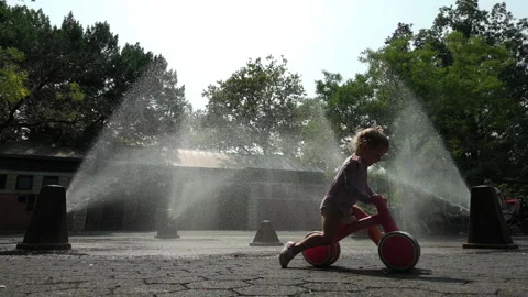 8-11-26, Brooklyn, NY, USA - slomo girl on tricycle rides thru sprinklers Stock Footage 341899127