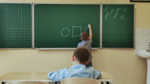 An 8-9 year old schoolboy draws figures with chalk on a blackboard Stock Footage 166549816