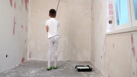 8 boy in white clothes holding a paint roller painting the walls of the room Video stock 268431297