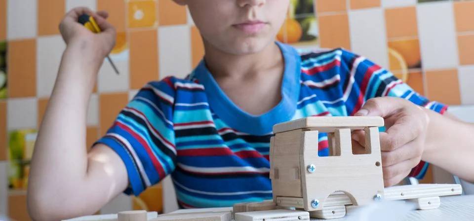 An 8-year-old boy assembles a wooden constructor by himself with a screwdri.. Stock Photos
