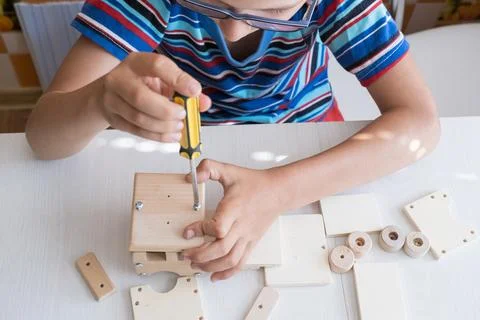 An 8-year-old boy assembles a wooden constructor by himself with a screwdri.. Foto stock