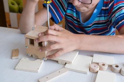 An 8-year-old boy assembles a wooden constructor by himself with a screwdri.. Stock-Fotos
