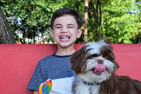 8 year old boy biting a lollipop and smiling at the camera, next to his pet. Stock Photos