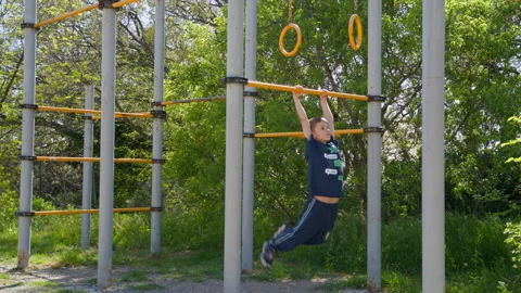 8-year-old boy doing pull-ups on outdoor bar, kids fitness and healthy lifestyle Stock Footage 308032351