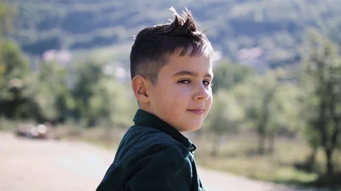 8-year-old boy looks into the camera against the backdrop of beautiful mountains Stock Footage 128066376