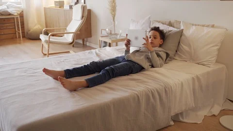 8 year old boy lying on a bed and using digital tablet computer Stock Footage 104227715