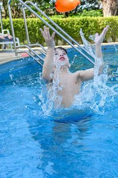 8 year old boy in the pool waiting to hold a water bomb that has been dropped. Stock Photos
