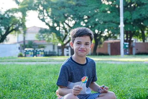 8 year old boy sitting on the lawn on a sunny afternoon, smiling and holding  Stock Photos